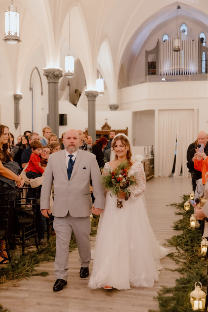 The bride walking down the aisle with her dad at Main Street Abbey. 